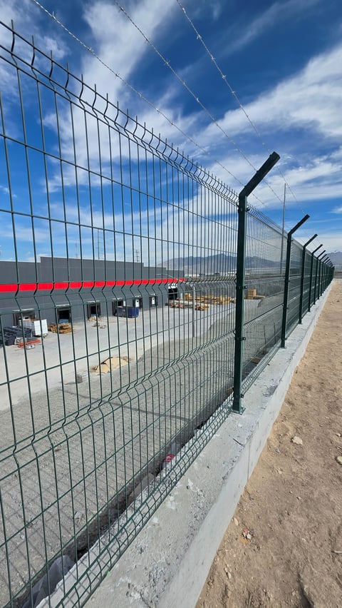Metal security fence with black posts along a construction site, blue sky and industrial building visible in background