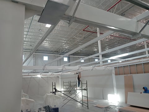 Interior construction site with exposed metal framework, temporary walls, and work scaffolding under industrial ceiling