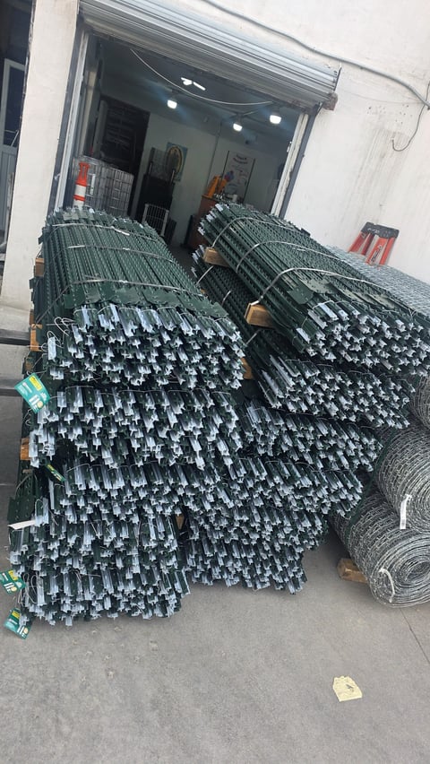 Large stacks of metal reinforcing bars stored outside a storefront, with rolls of mesh fencing visible on the right
