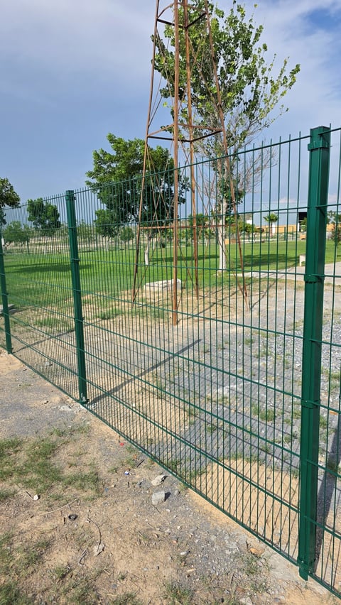 Open green metal gate with climbing vines attached to a wooden pole in a fenced recreational area