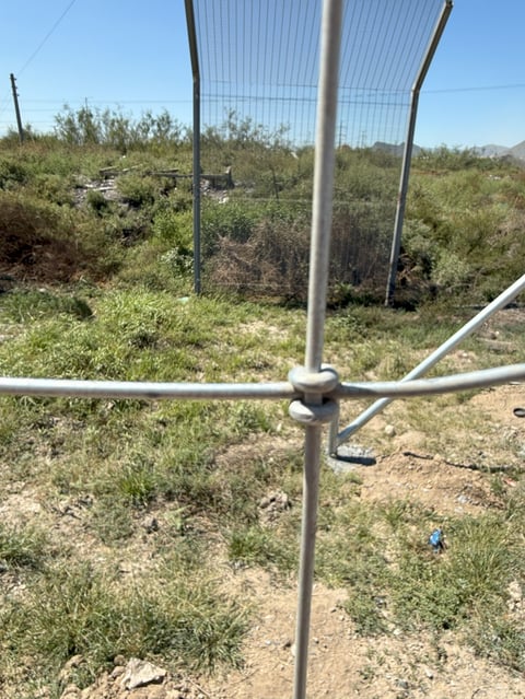 Metal security gate frame in desert landscape with sparse vegetation and mountains in background under clear sky
