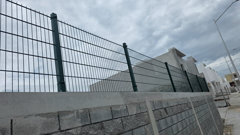 Black metal fencing with concrete base along a paved area under overcast sky